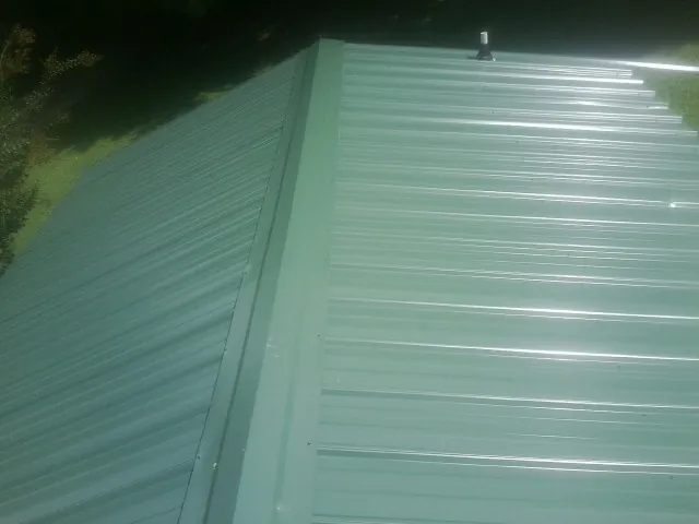 New green metal panels meeting at the ridge of a roof — Flat Roof Repair work by our crew in Henrico
