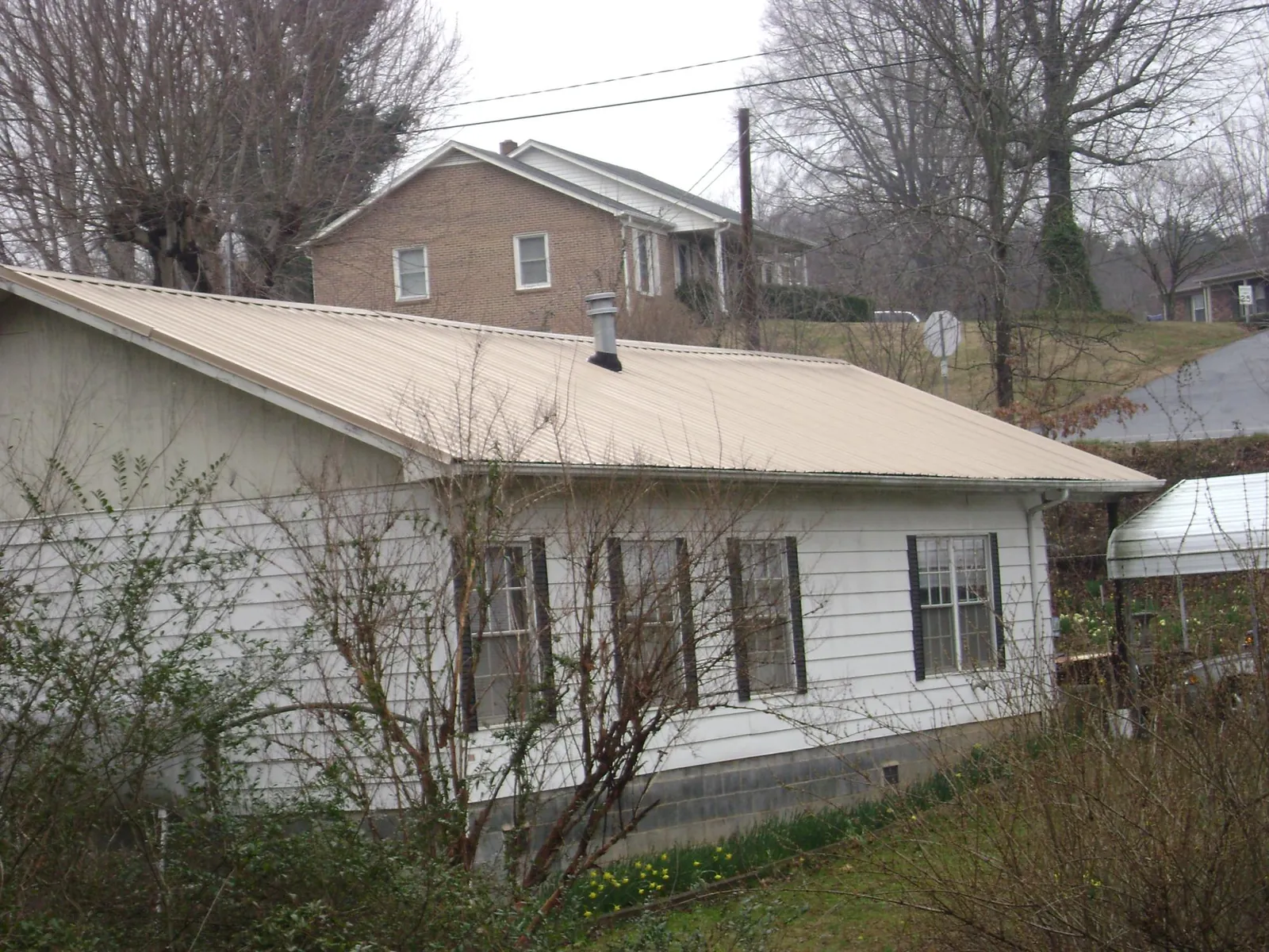 Tan metal roof on a white sided house set into a hillside — Commercial Roofing by Roofing Brothers in Henrico
